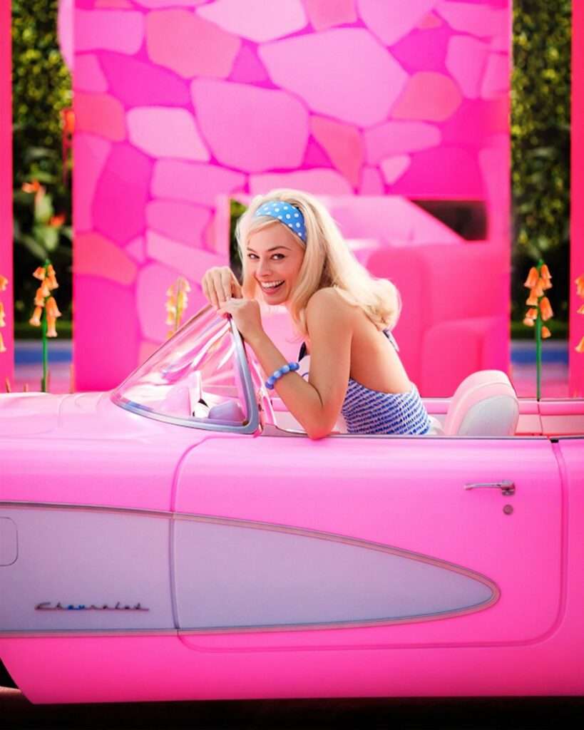 Margot Robbie as Barbie in a pink Barbie car