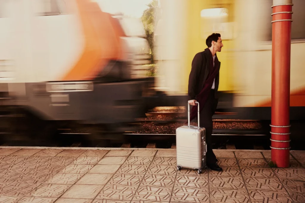 Adrien Brody with a suitcase on a train station platform.