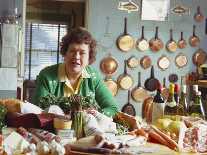 Julia Child in the kitchen with food and copper cookware.